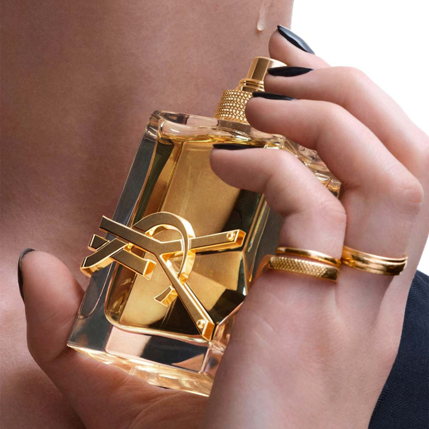 Frasco do YSL Libre sendo segurado por mão feminina com anéis e unhas pretas, próximo ao pescoço, transmitindo elegância e sensualidade.