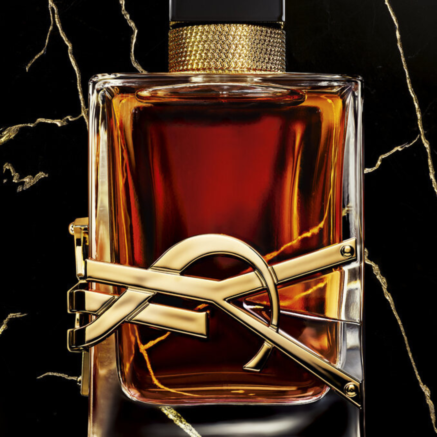 Close-up do frasco do perfume Libre Saint Laurent Le Parfum em um fundo escuro com veias douradas, realçando o brilho do líquido âmbar e o logo "YSL" dourado, enfatizando a sofisticação e a intensidade da fragrância.