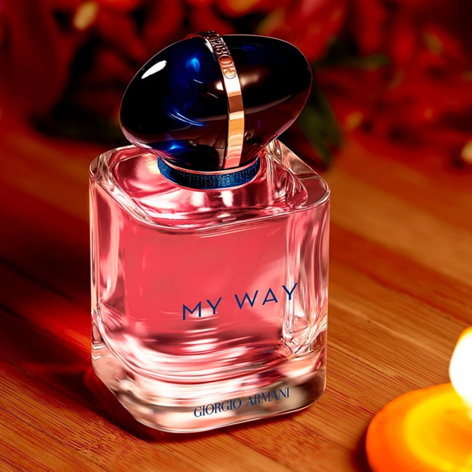 Perfume My Way Giorgio Armani inclinado sobre uma superfície de madeira clara com uma luz suave e quente incidindo, com um fundo avermelhado e parte de uma vela à direita, criando uma atmosfera acolhedora e sofisticada.