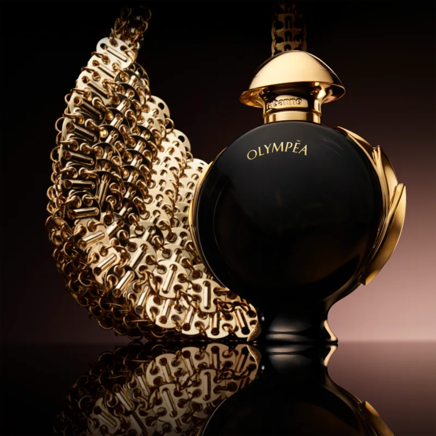Perfume importado feminino Olympéa Parfum Rabanne posicionado ao lado de uma corrente dourada elaborada, refletindo em uma superfície escura, sugerindo uma aura de força e sofisticação dourada, disponível na Velyre.