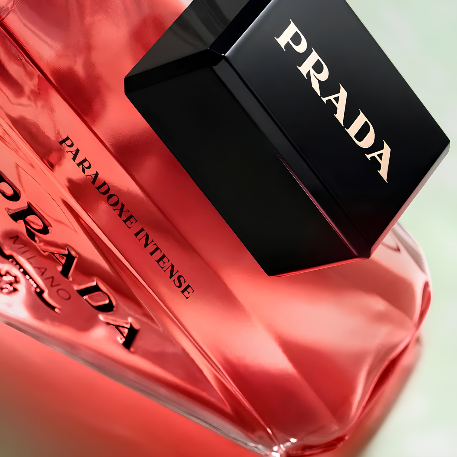 Close-up do frasco do perfume Paradoxe Intense Prada, focado no logo "PRADA" e na inscrição "PARADOXE INTENSE", com a tampa preta angulada ao lado, realçando o design moderno e sofisticado.