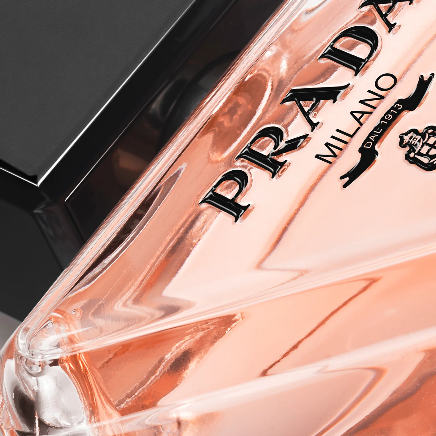 Close-up do frasco do perfume Paradoxe Prada, focando no logo "PRADA MILANO DAL 1913" em preto sobre o líquido rosa claro, realçando a marca e a sofisticação do design.