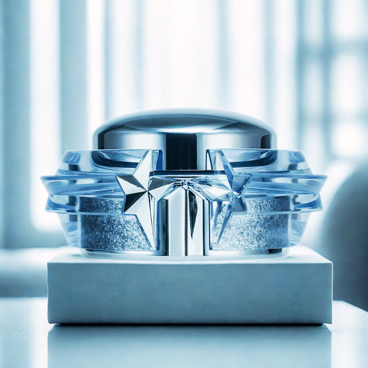Pote da pasta hidratante perfumada Angel Mugler Perfuming Body Cream em destaque sobre um pedestal branco, com um fundo desfocado em tons de azul e branco, transmitindo uma aura de brilho e luxo.