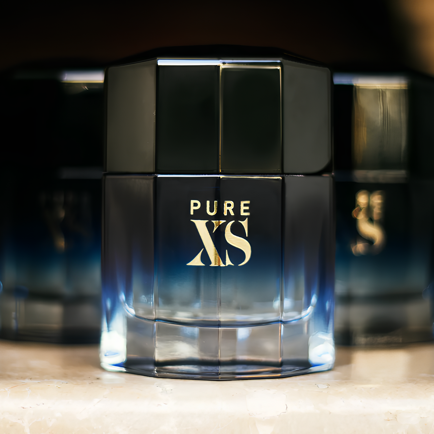 Perfume masculino Pure XS Rabanne em destaque em uma prateleira escura, com outros frascos similares desfocados ao fundo, sugerindo uma coleção de fragrâncias masculinas intensas.