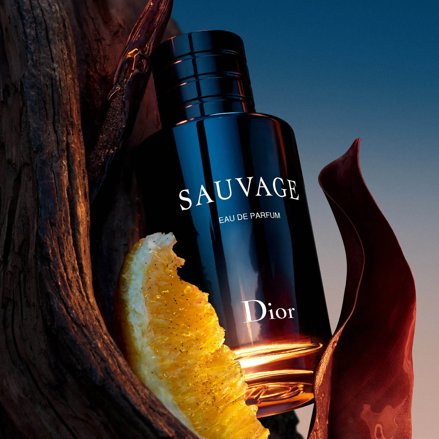 Perfume Sauvage Dior posicionado entre pedaços de madeira escura e uma fatia de laranja, com um fundo azul e tons quentes, sugerindo as notas amadeiradas e cítricas da fragrância.
