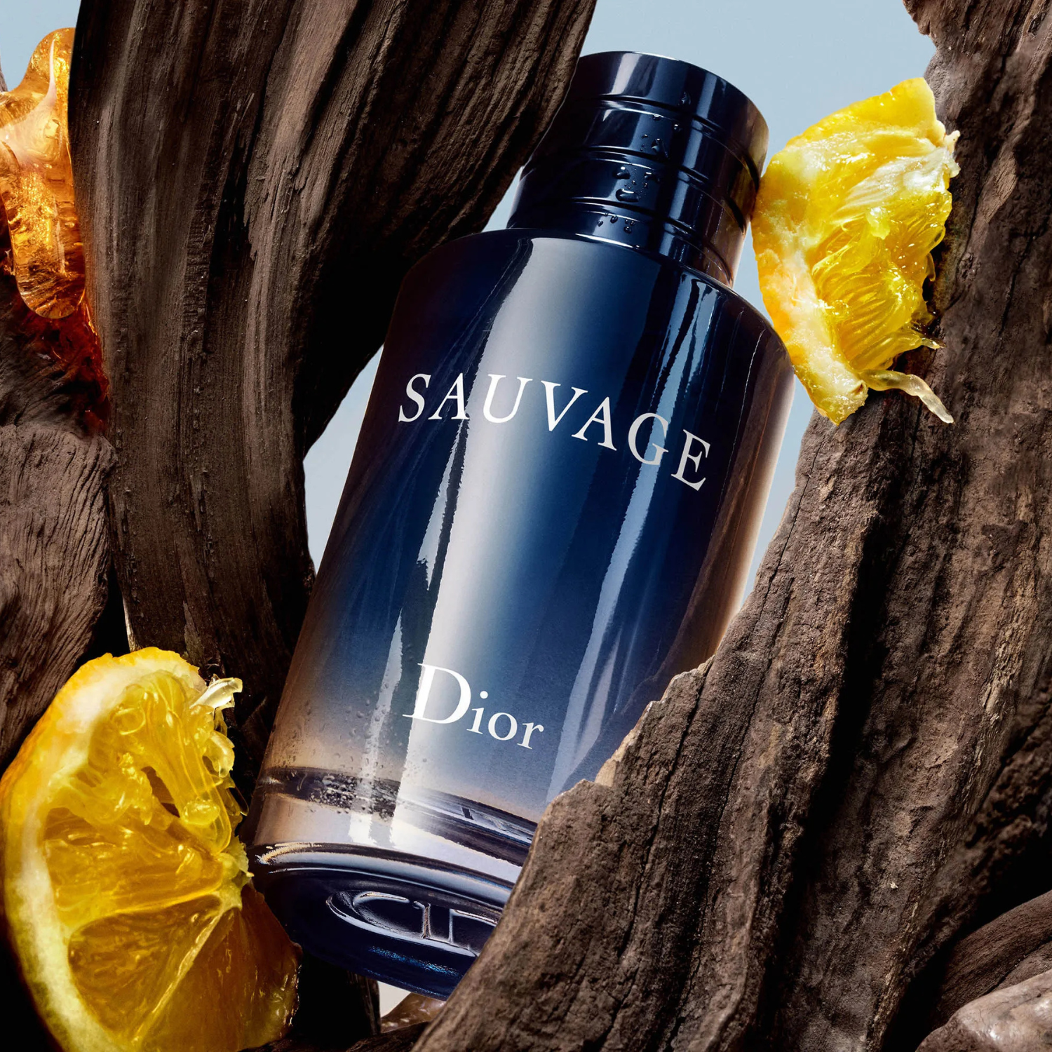 Perfume Sauvage Dior inclinado em um cenário com pedaços de madeira escura e duas metades de laranja, sugerindo uma combinação de notas amadeiradas e cítricas, representando a natureza bruta e fresca.