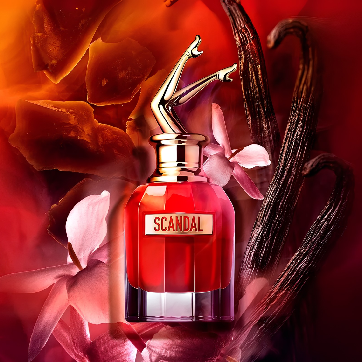 Perfume Scandal Le Parfum de Jean Paul Gaultier posicionado entre flores rosadas, favas de baunilha e cristais de âmbar, sobre fundo vibrante em tons de vermelho e laranja.