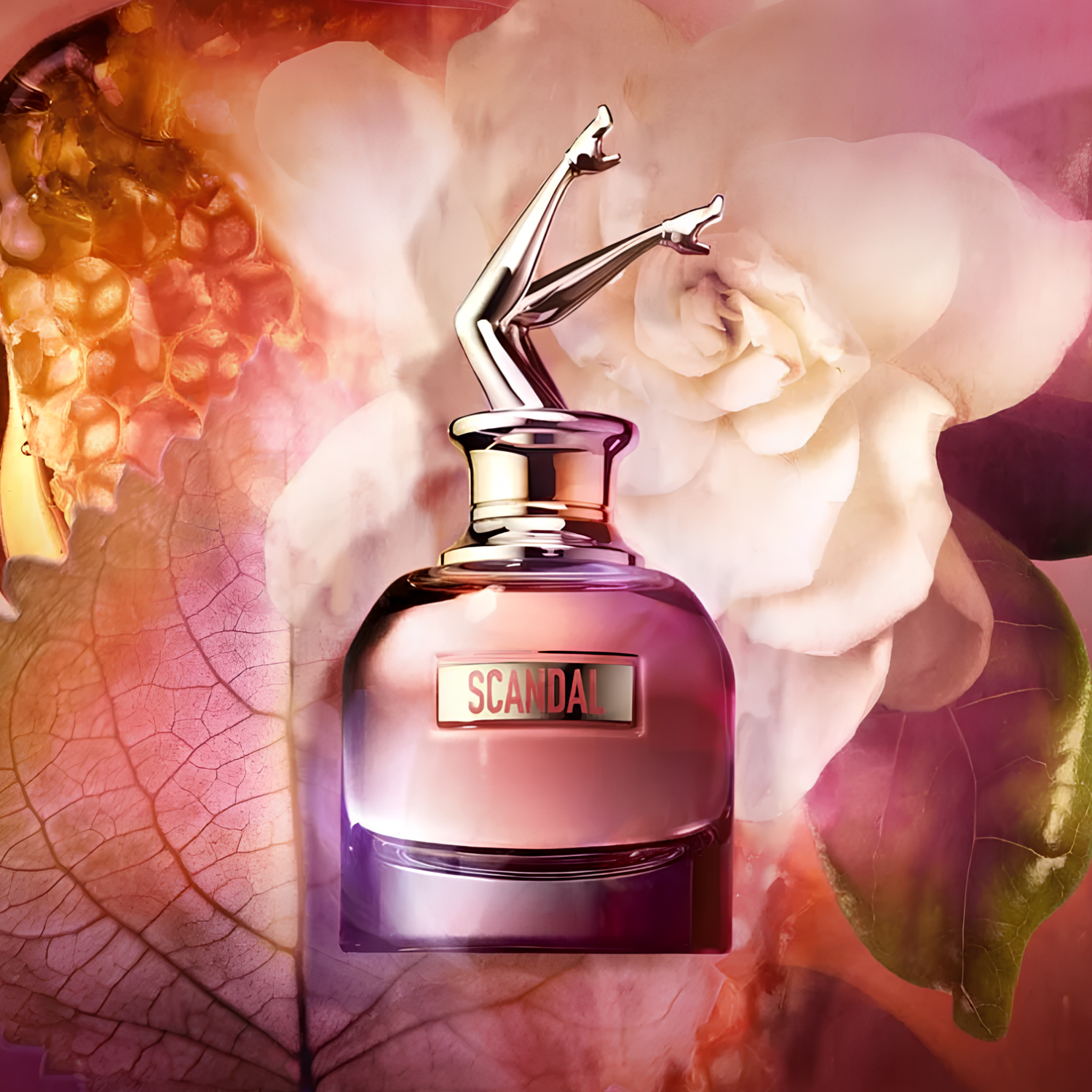 Perfume Scandal Jean Paul Gaultier posicionado sobre fundo floral com pétalas brancas, folhas secas e colmeia dourada. O frasco reflete tons rosados sob luz suave, transmitindo feminilidade e doçura.