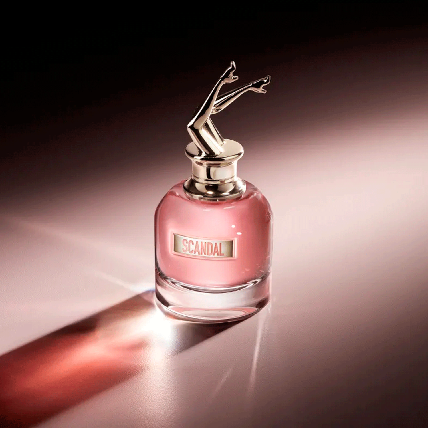 Perfume Scandal Jean Paul Gaultier em superfície clara com iluminação lateral intensa, projetando sombra em tons rosados. O frasco brilha com elegância e sensualidade.