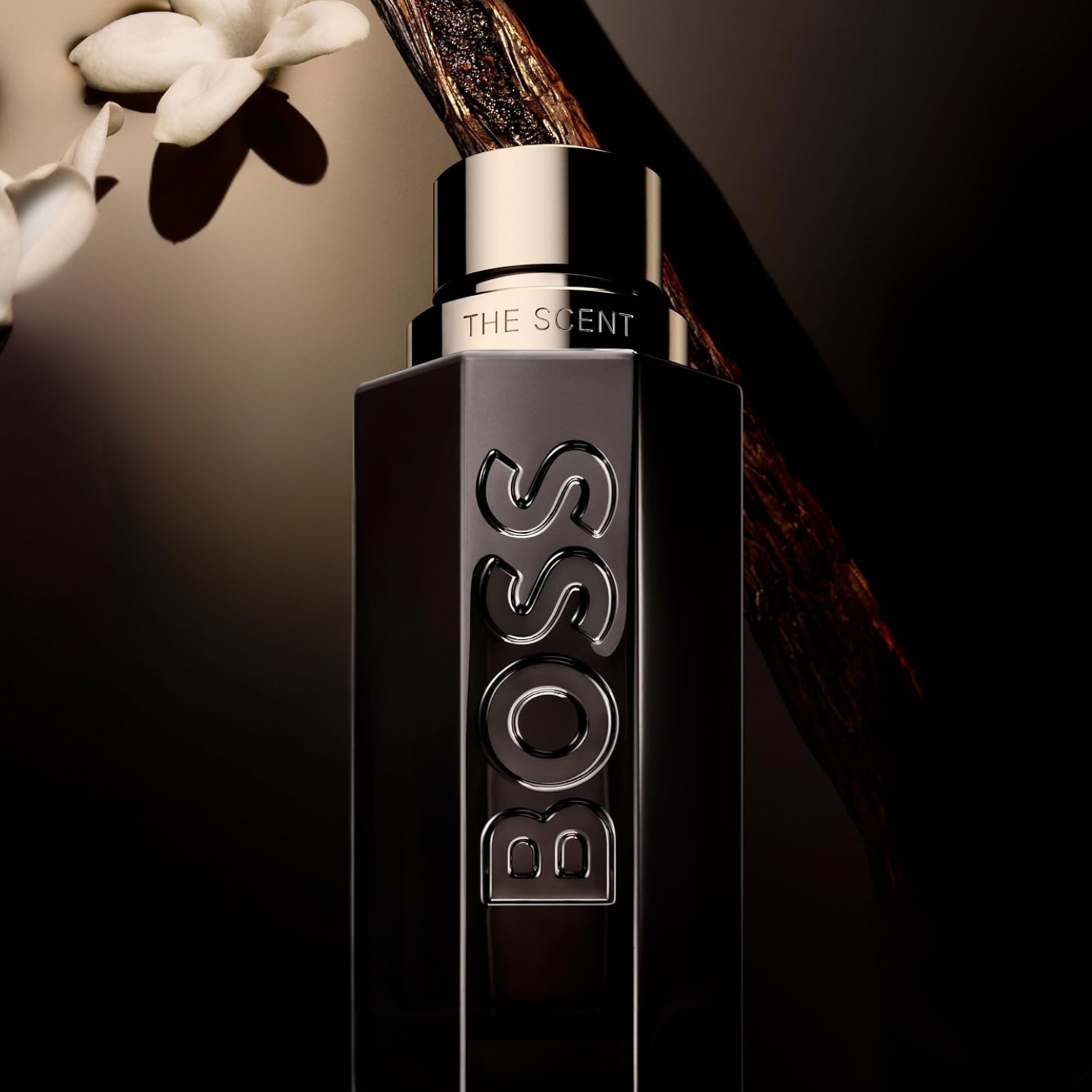 Perfume Boss The Scent Magnetic da Hugo Boss em cenário escuro com vagem de baunilha e flor branca ao fundo, reforçando sua assinatura olfativa sedutora e envolvente.