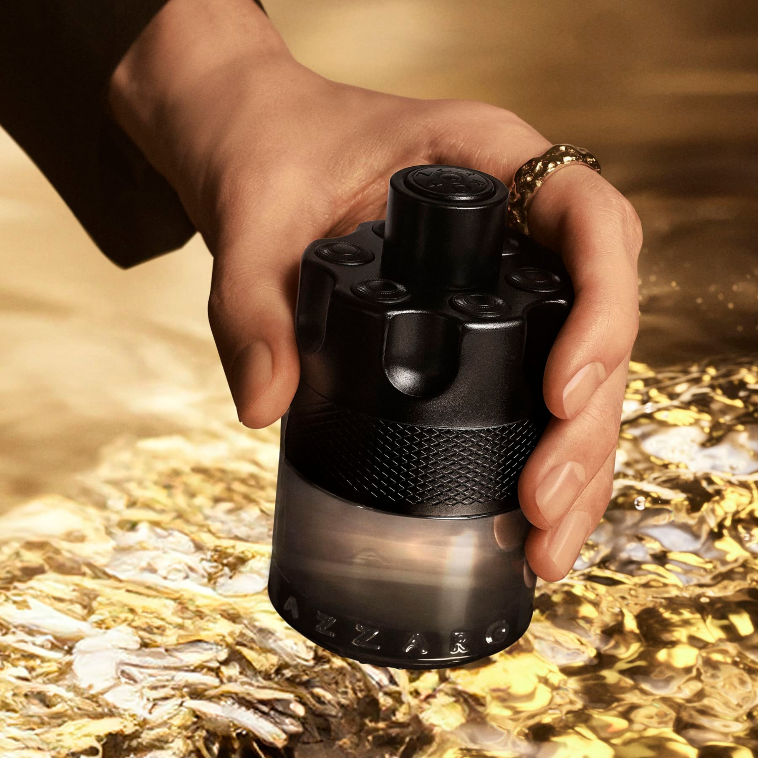 Mão de um homem segurando o frasco do perfume The Most Wanted Azzaro contra um fundo dourado e brilhante, evocando uma fragrância para o homem confiante e sedutor.