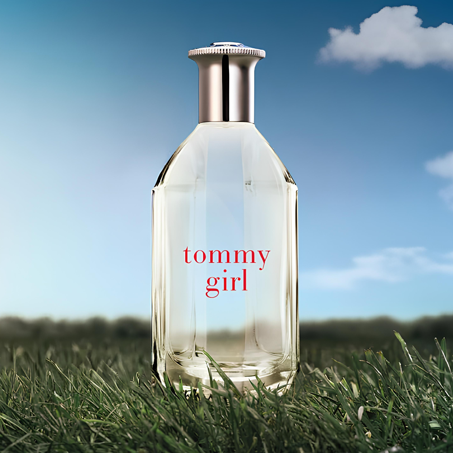 Perfume Tommy Girl Tommy Hilfiger em destaque em um campo de grama verde com um céu azul e nuvens ao fundo, transmitindo uma sensação de frescor, liberdade e natureza.
