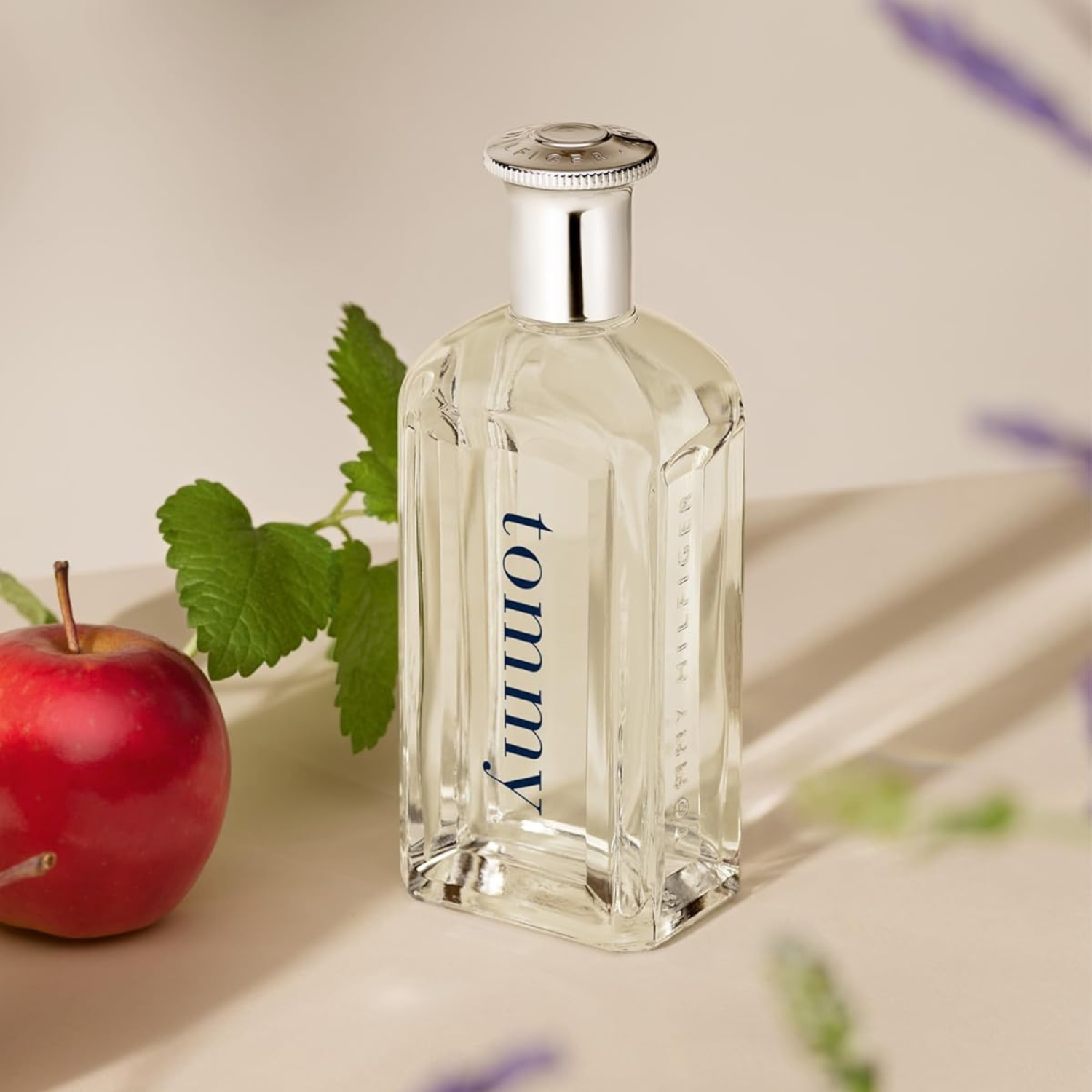 Perfume masculino Tommy Men Tommy Hilfiger em destaque ao lado de uma maçã vermelha e um ramo de hortelã, evocando uma fragrância frutada, fresca e herbácea, com uma atmosfera natural.