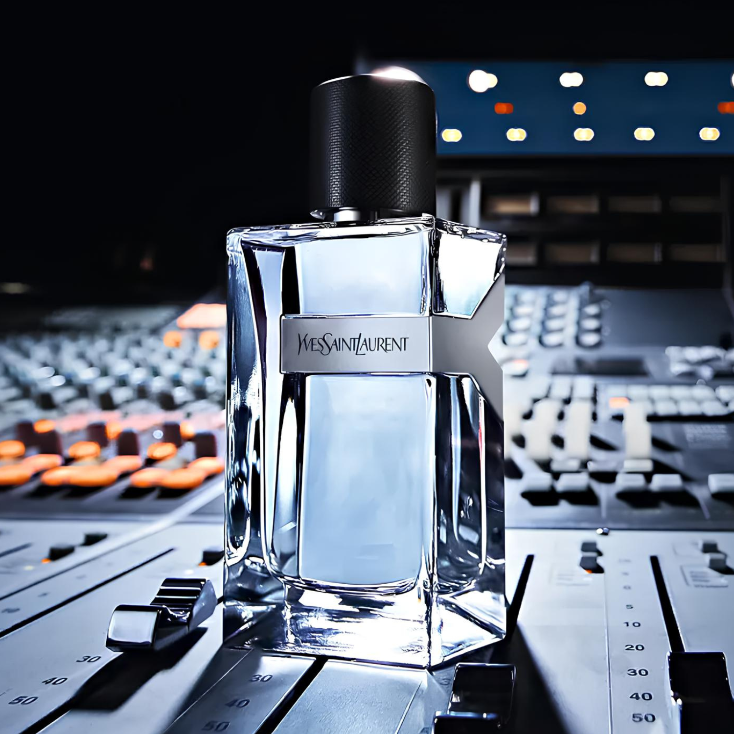 Perfume Y Yves Saint Laurent posicionado sobre uma mesa de som profissional em um estúdio, com luzes e botões visíveis, sugerindo uma fragrância para o homem criativo e moderno.